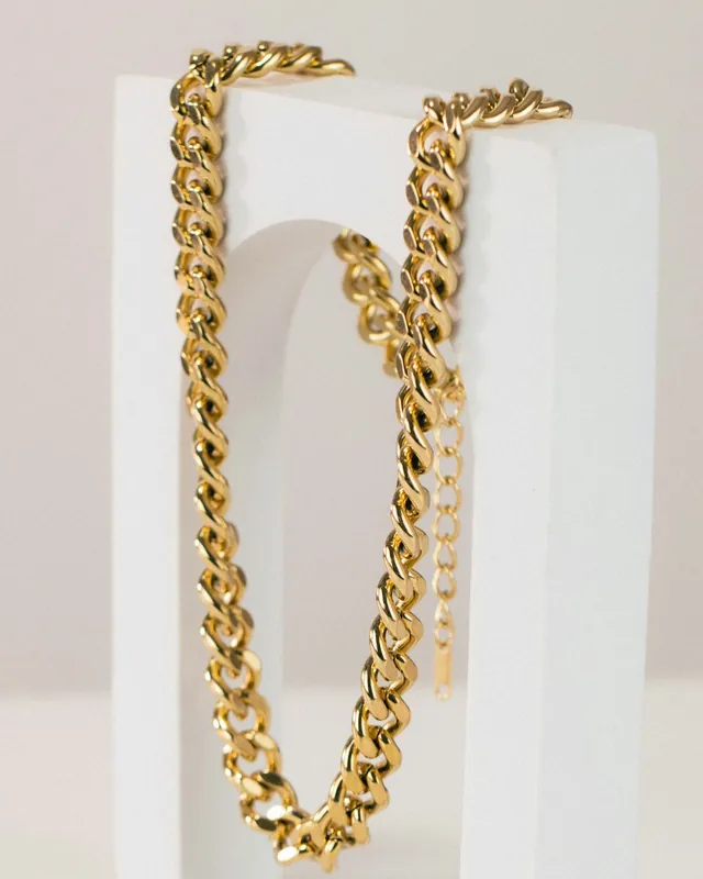 Gold Cuban link chain draped over a white stand