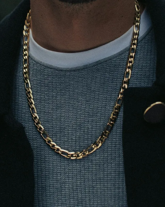 Gold Figaro chain worn over a grey sweater